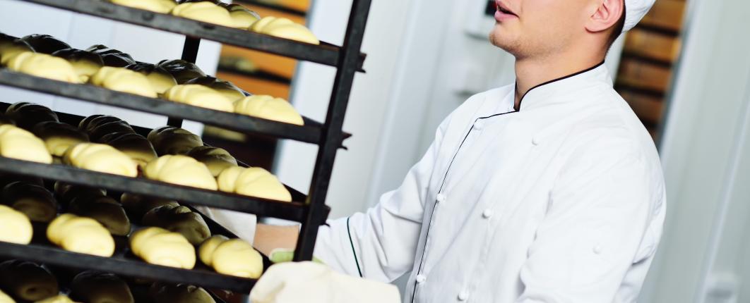 Jeune homme boulanger qui pousse un présentoir avec des croissants 