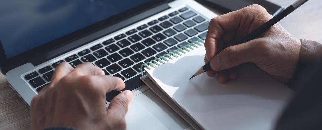 Personne qui écrit une calepin posé sur un clavier de PC