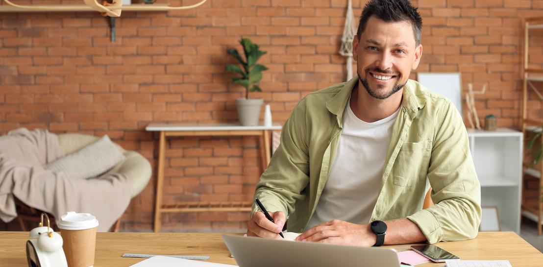une personne sourit assis à une table avec un ordinateur