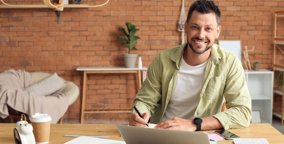 une personne sourit assis à une table avec un ordinateur