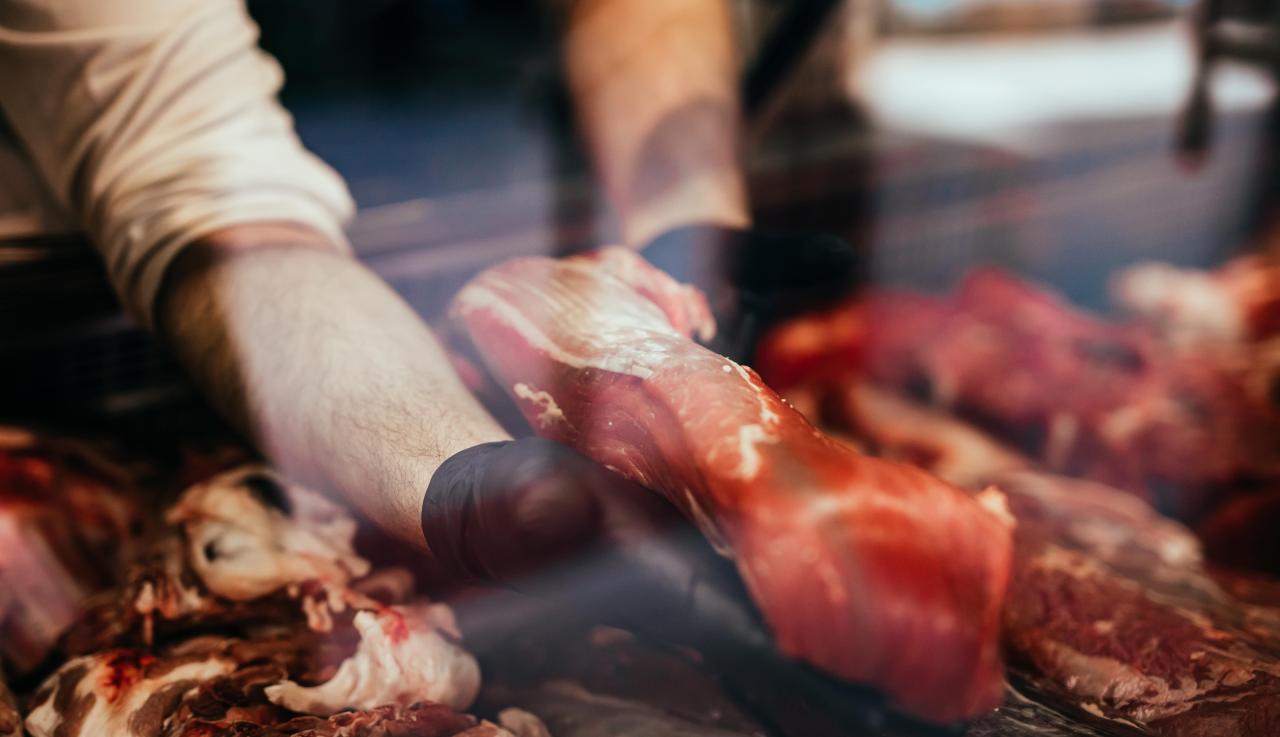 Boucher tenant un morceau de viande dans ses mains à travers la vitrine d'une étale de boucherie