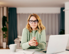 Une femme avec des lunettes assise devant un ordi et une tasse 