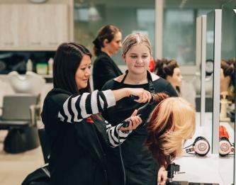 une apprentie coiffe une pérruque en cours