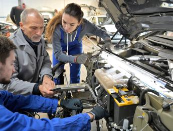Plusieurs mécaniciens qui œuvrent dans un capot de voiture ouvert 