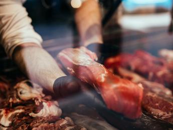 Boucher tenant un morceau de viande dans ses mains à travers la vitrine d'une étale de boucherie