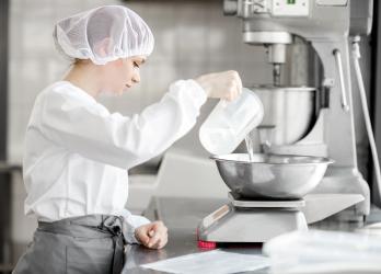 Jeune fille avec une charlotte dans les cheveux en train de verser un liquide dans une préparation en cuisine