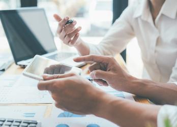 Deux personnes qui regardent une tablette, des graphiques sont imprimés sur des feuilles posées sur un bureau
