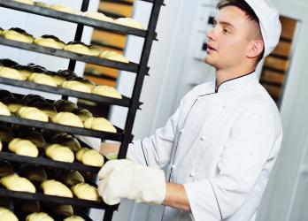 Jeune homme boulanger qui pousse un présentoir avec des croissants 