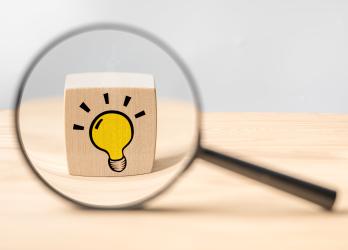 Image d'une loupe qui grossit un dés avec un dessin d'ampoule dessus