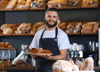 Un homme dans une boulangerie entouré de pain tient une tarte 