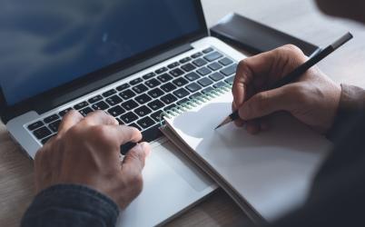 Personne qui écrit une calepin posé sur un clavier de PC