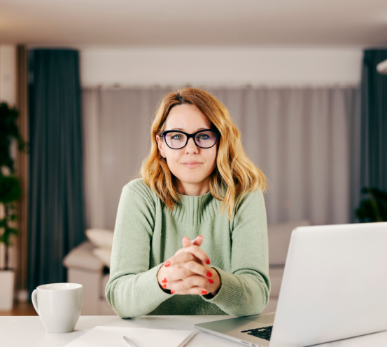 Une femme avec des lunettes assise devant un ordi et une tasse 