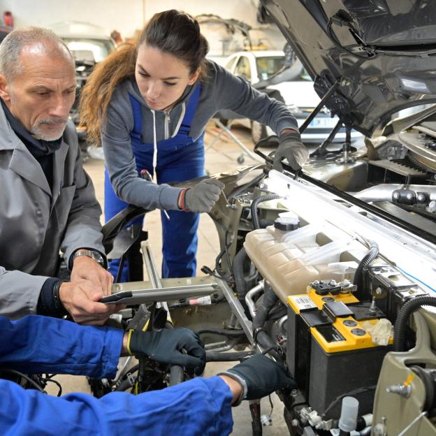 Plusieurs mécaniciens qui œuvrent dans un capot de voiture ouvert 