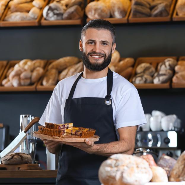 Un homme dans une boulangerie entouré de pain tient une tarte 
