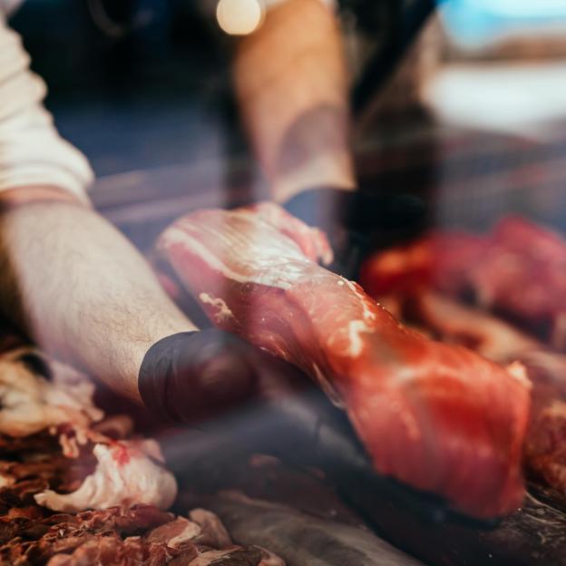 Boucher tenant un morceau de viande dans ses mains à travers la vitrine d'une étale de boucherie
