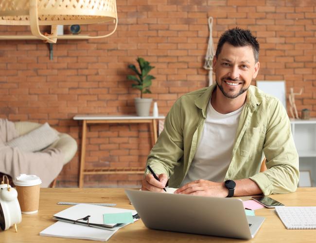 une personne sourit assis à une table avec un ordinateur