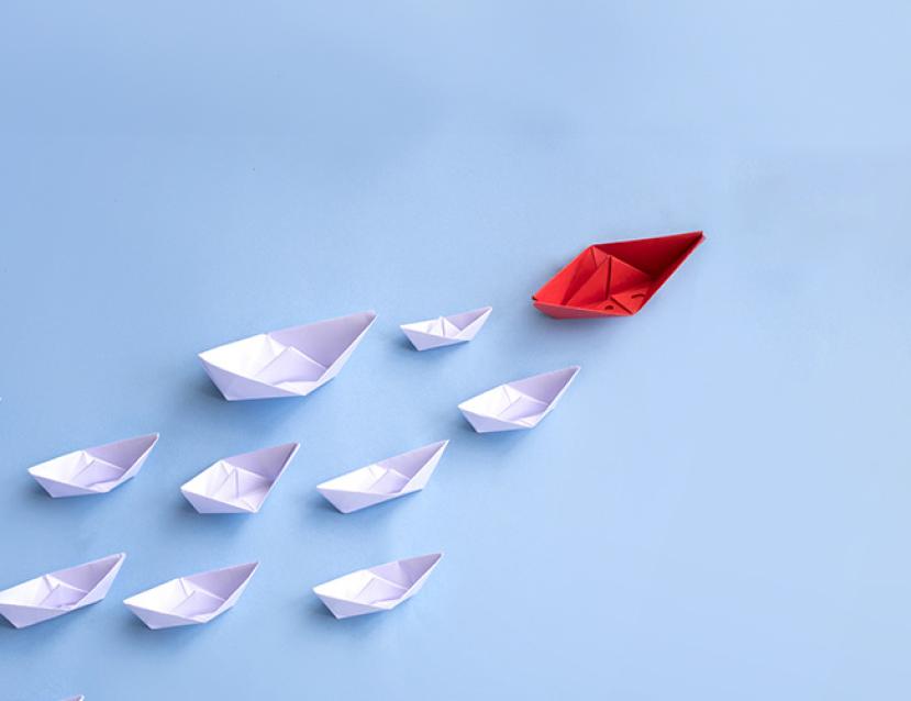 Photo illustrative d'un bateau en papier rouge qui embarque les autres bateaux tel un leader