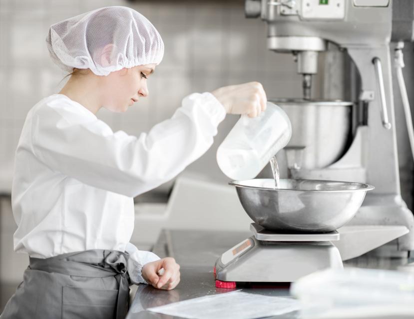 Jeune fille avec une charlotte dans les cheveux en train de verser un liquide dans une préparation en cuisine