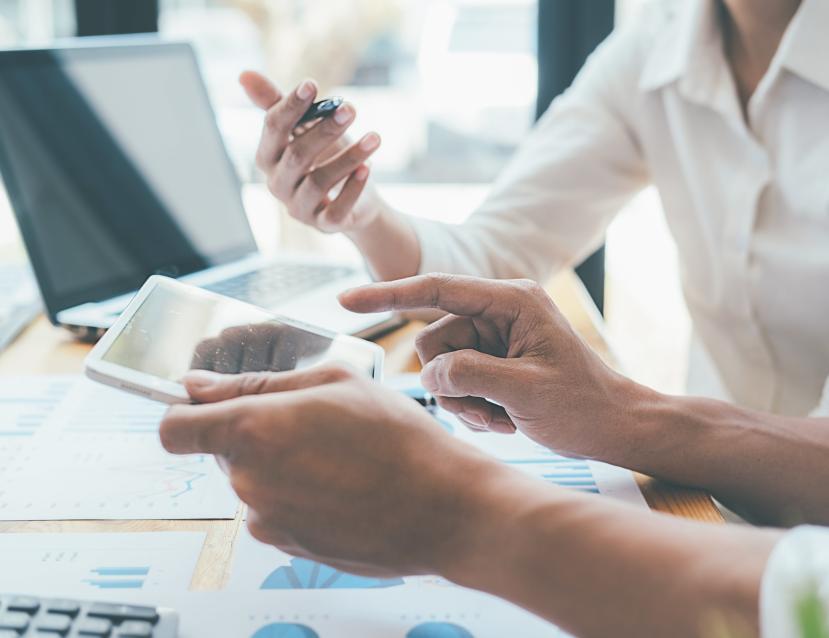 Deux personnes qui regardent une tablette, des graphiques sont imprimés sur des feuilles posées sur un bureau
