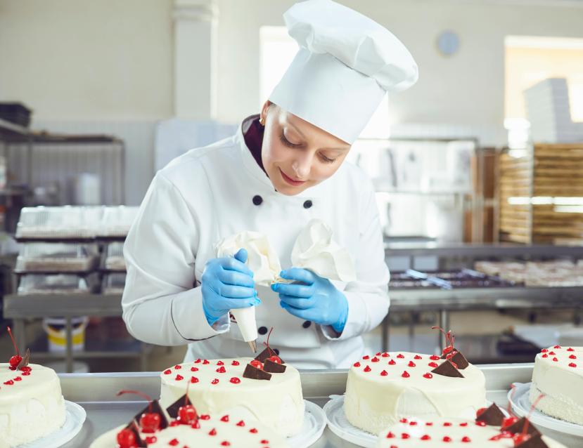 Jeune pâtissière en train de décorer des gâteaux avec une poche à douille
