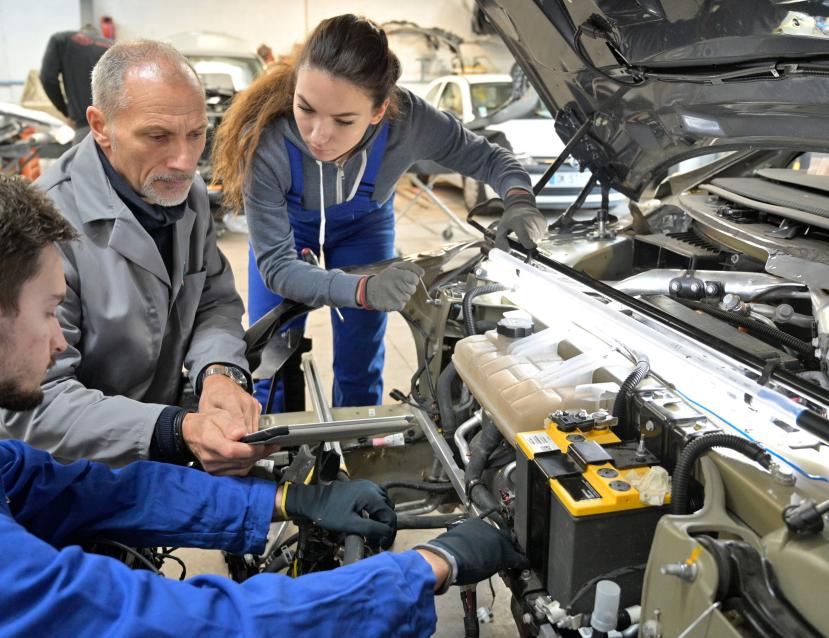 Plusieurs mécaniciens qui œuvrent dans un capot de voiture ouvert