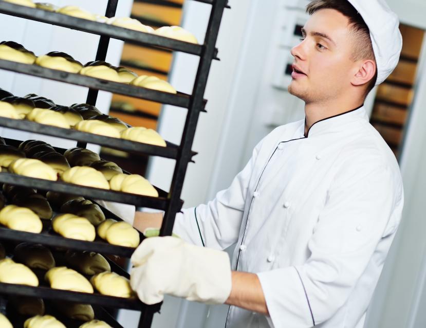 Jeune homme boulanger qui pousse un présentoir avec des croissants