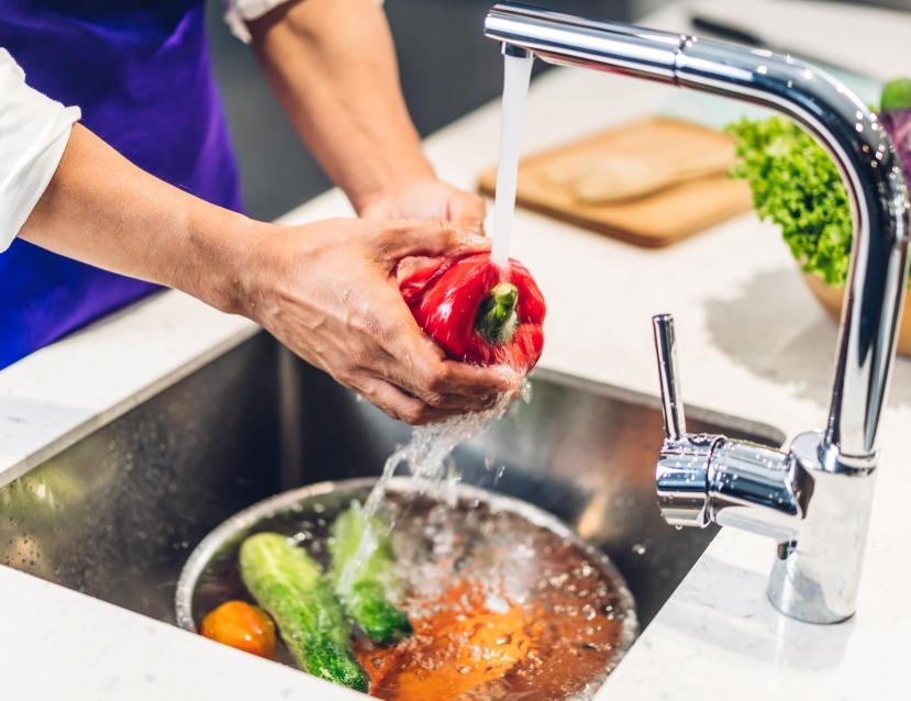 Personne qui lave des légumes dans un évier