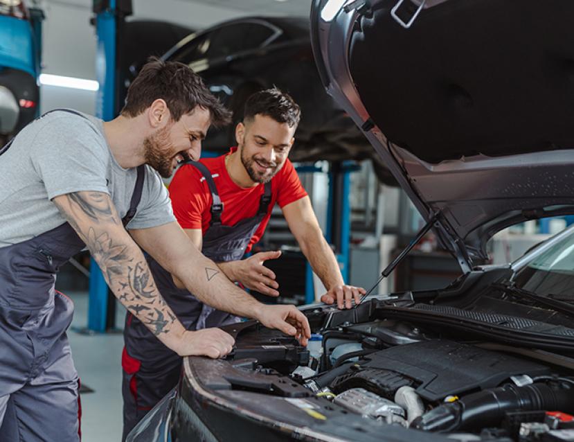 Photo d'un apprenti mécanicien et son tuteur devant le moteur d'un voiture