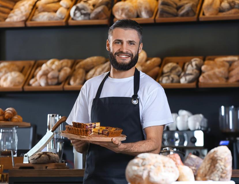 Un homme dans une boulangerie entouré de pain tient une tarte 