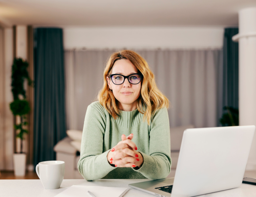 Une femme avec des lunettes assise devant un ordi et une tasse 